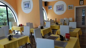 Ein Essbereich mit Tischen, die gelb gedeckt sind, Stühlen und gerahmten Bildern an den Wänden.