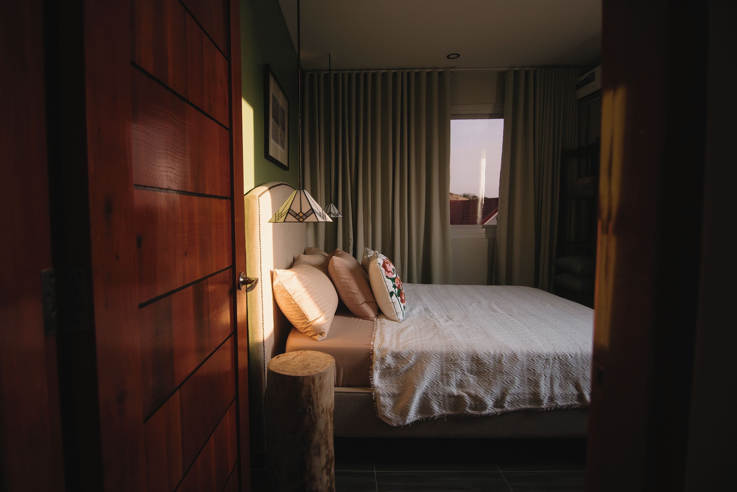 A bedroom with a bed, a wooden wardrobe, a window with curtains, and a bedside table.