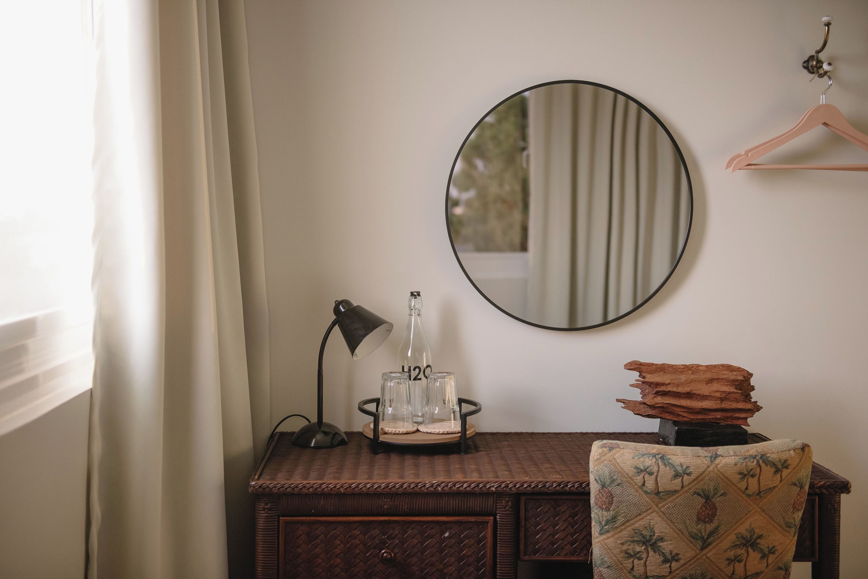 Una habitación con un espejo redondo, un escritorio con una lámpara, una botella y una silla.