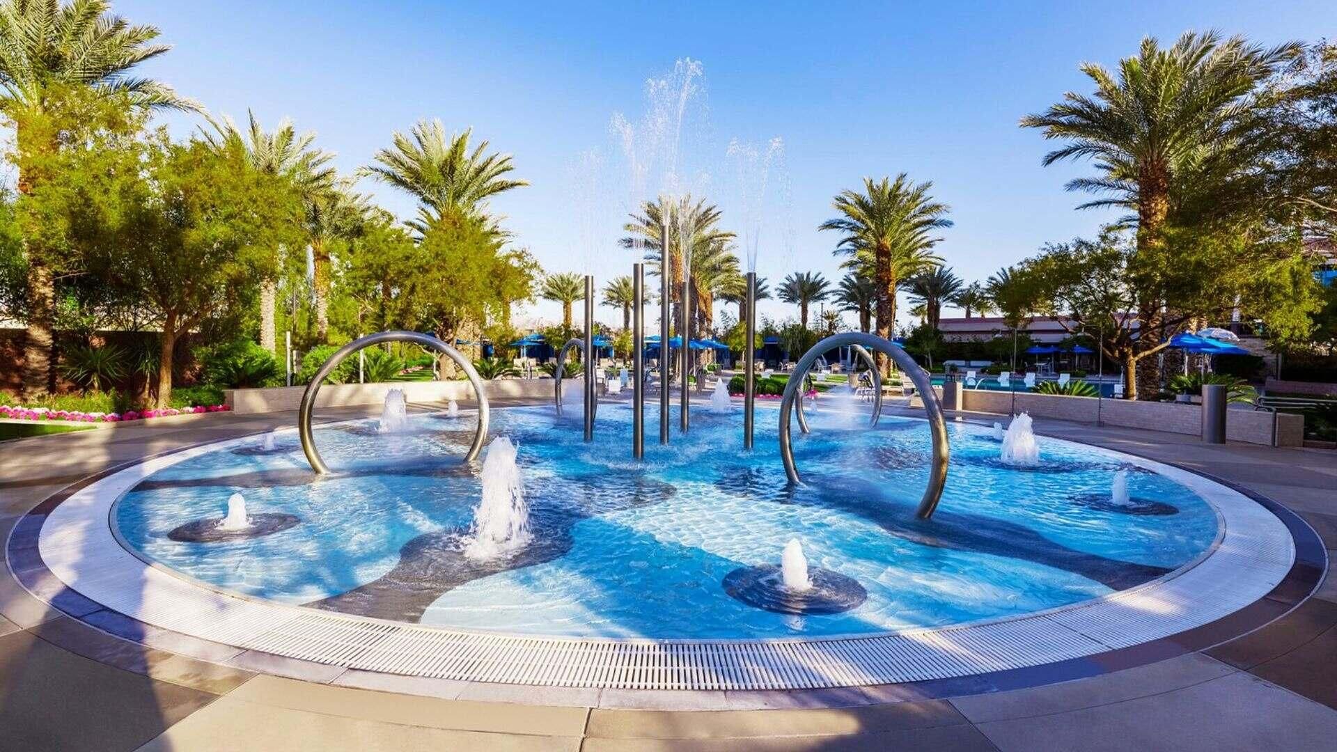 Una piscina circular con varias fuentes y palmeras a su alrededor.