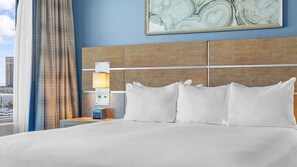 Een hotelkamer met een groot bed, een nachtkastje met een lamp en uitzicht op een stadslandschap door het raam.