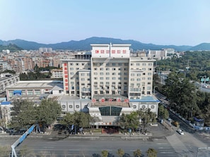 Um hotel moderno de vários andares, situado numa área urbana com vista para montanhas ao longe.