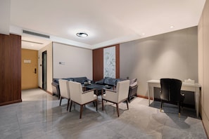 Quarto de hotel moderno com área de jantar, sofá, escrivaninha e cadeira.