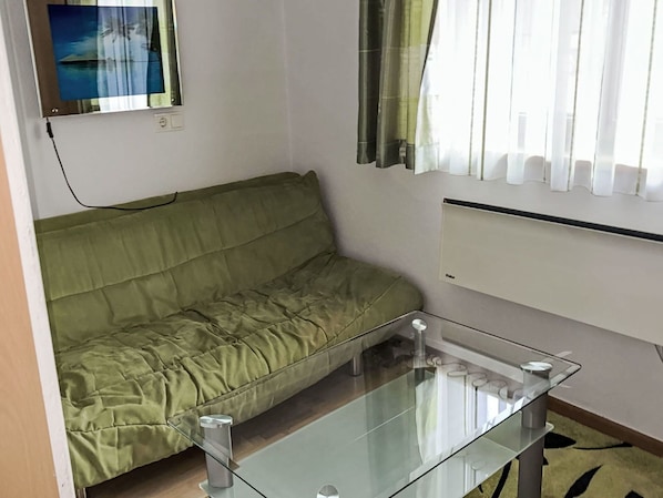 A room with a green sofa, a glass coffee table, a wall-mounted radiator, and a window with curtains.