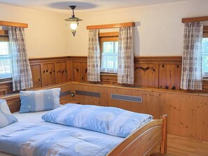 A wooden-paneled room with a bed, two windows with curtains, a ceiling light fixture, and a wooden bench. - Beautiful  villa for 2 people with WIFI, TV and balcony (Wildschönau)
