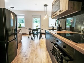 Eine moderne Küche mit einer zentralen Kochinsel, Holzböden und Blick ins Freie durch große Fenster.