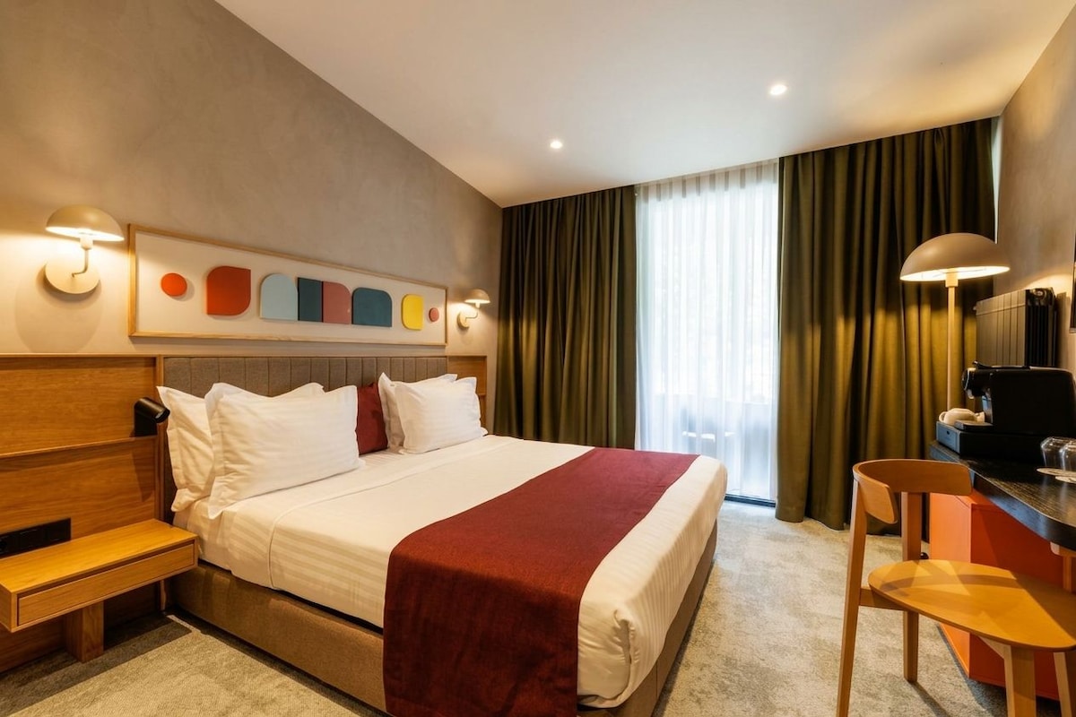 Una habitación de hotel con cama, mesita de noche, lámpara y un escritorio con silla.