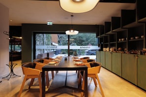 Un interior de restaurante con una larga mesa de comedor, sillas y vistas a través de las ventanas.