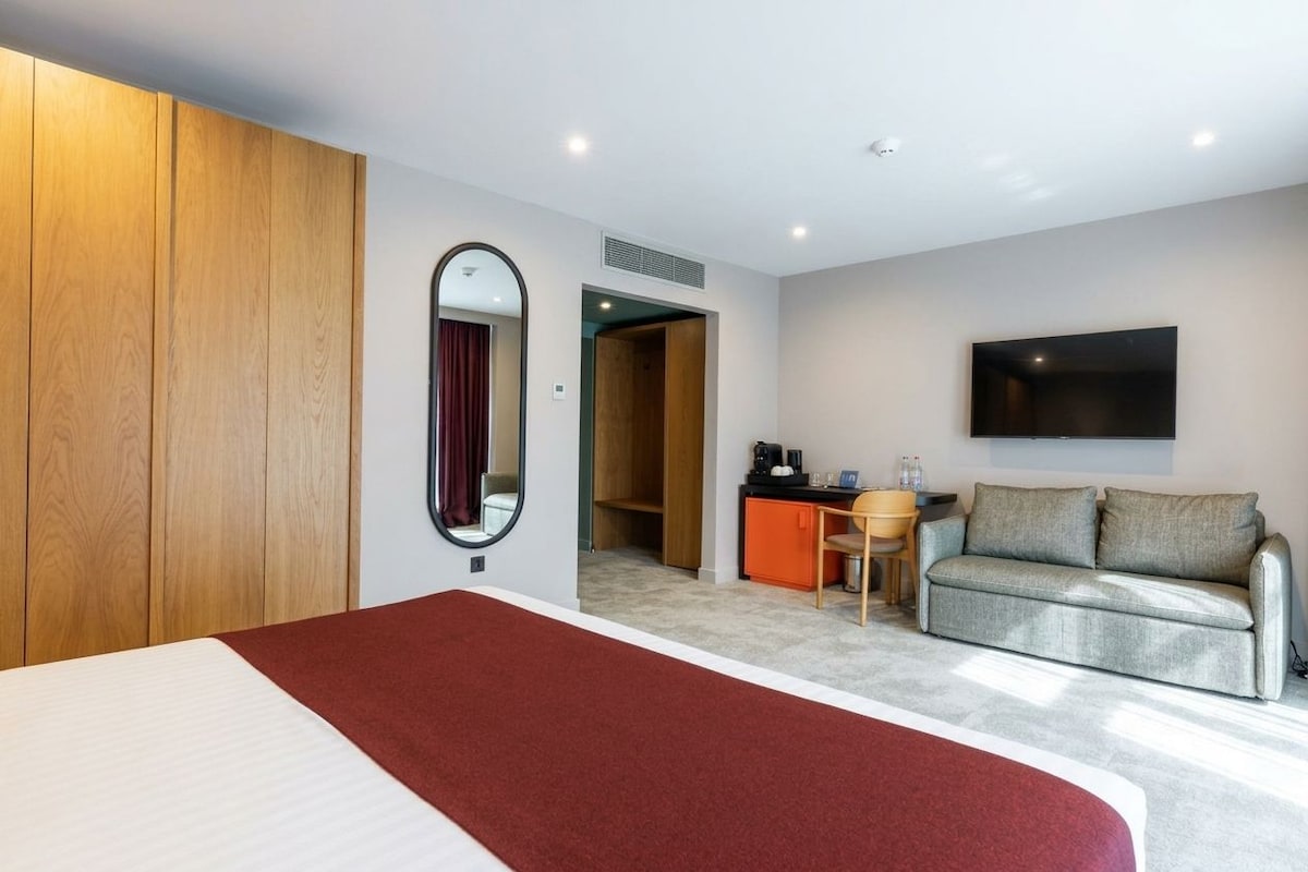 Habitación de hotel con cama, sofá, televisor montado en la pared y escritorio con silla.