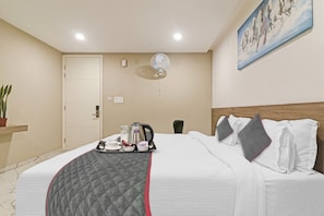 Ein Hotelzimmer mit einem Bett, einem Nachttisch mit Wasserkocher und Tee-Set, einem Wandventilator und einem Gemälde von Pferden.