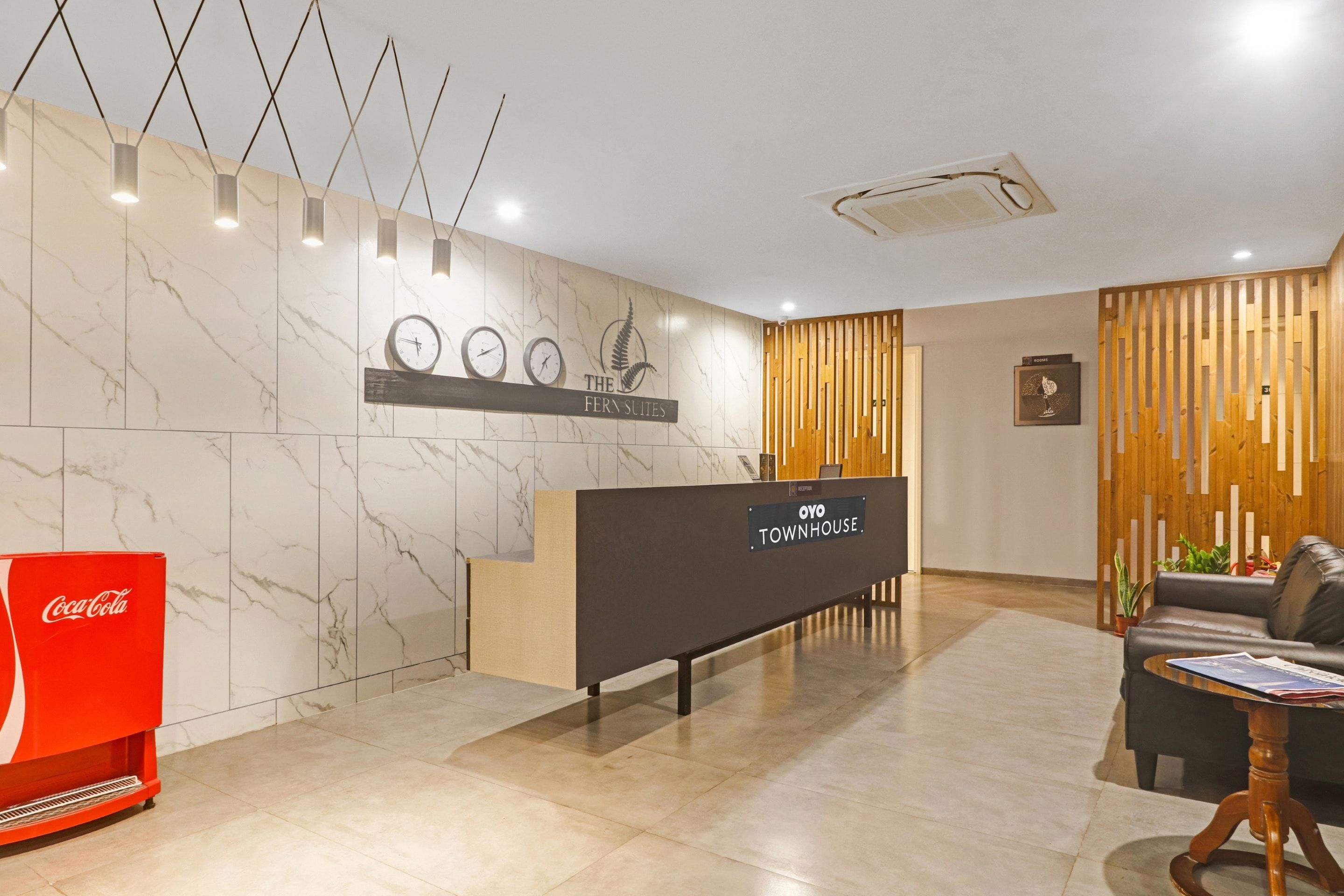 Zona de recepción de hotel con mostrador, relojes y logotipo de una planta de helecho.