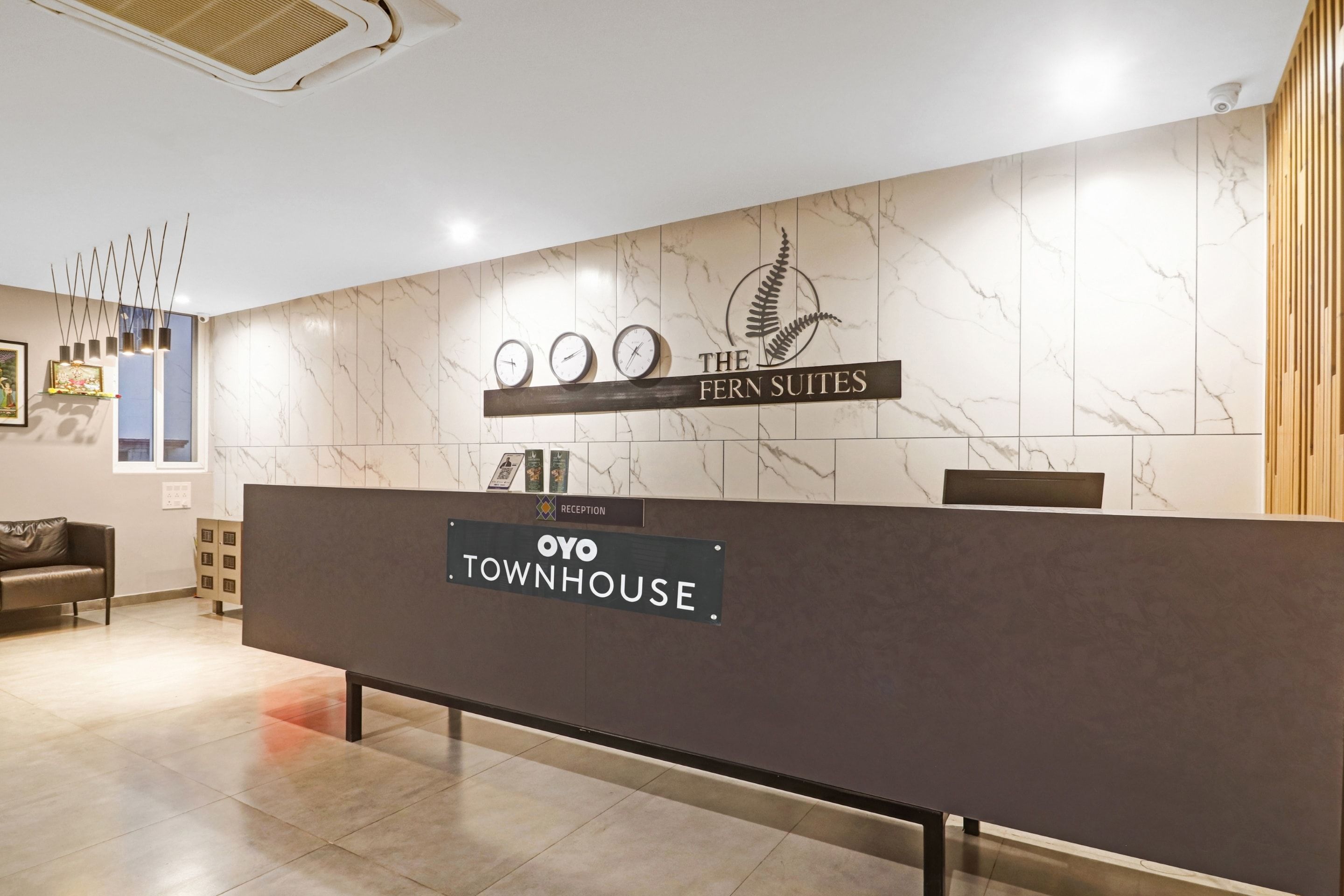 Bancada de recepção com placas indicando 'The Fern Suites' e hotel 'Oyo Townhouse'.