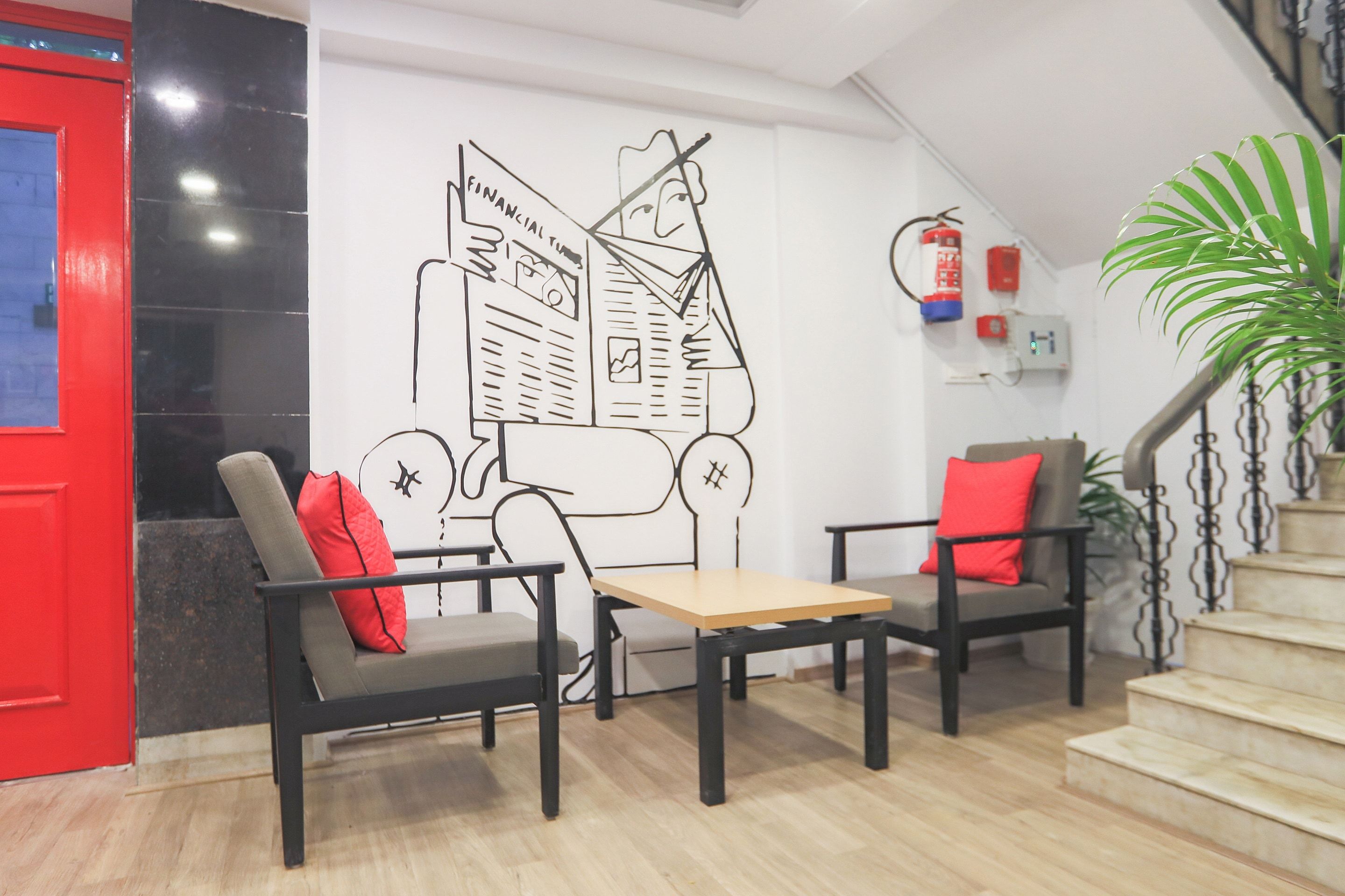 Um interior moderno com duas cadeiras pretas com almofadas vermelhas, uma mesa de madeira e um mural grande na parede.