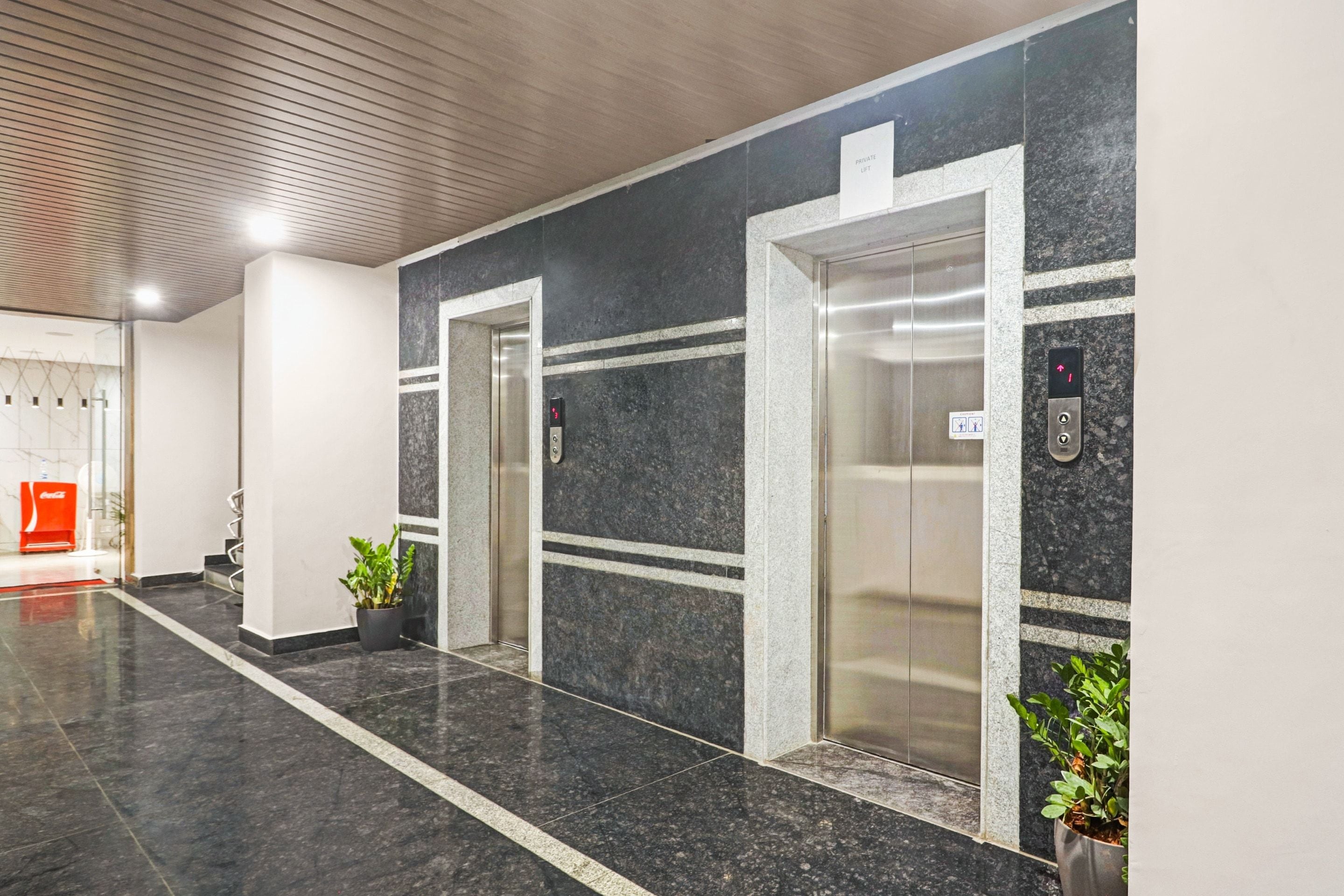 A modern elevator area with two elevators, marble flooring, and potted plants.