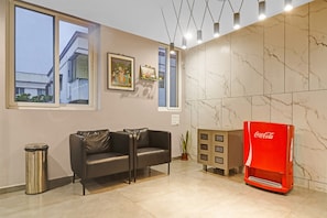 Ein modernes Wohnzimmer mit einer Couch, einem Mülleimer, einem roten Coca-Cola Kühlschrank und einem großen Fenster mit Blick auf Gebäude.