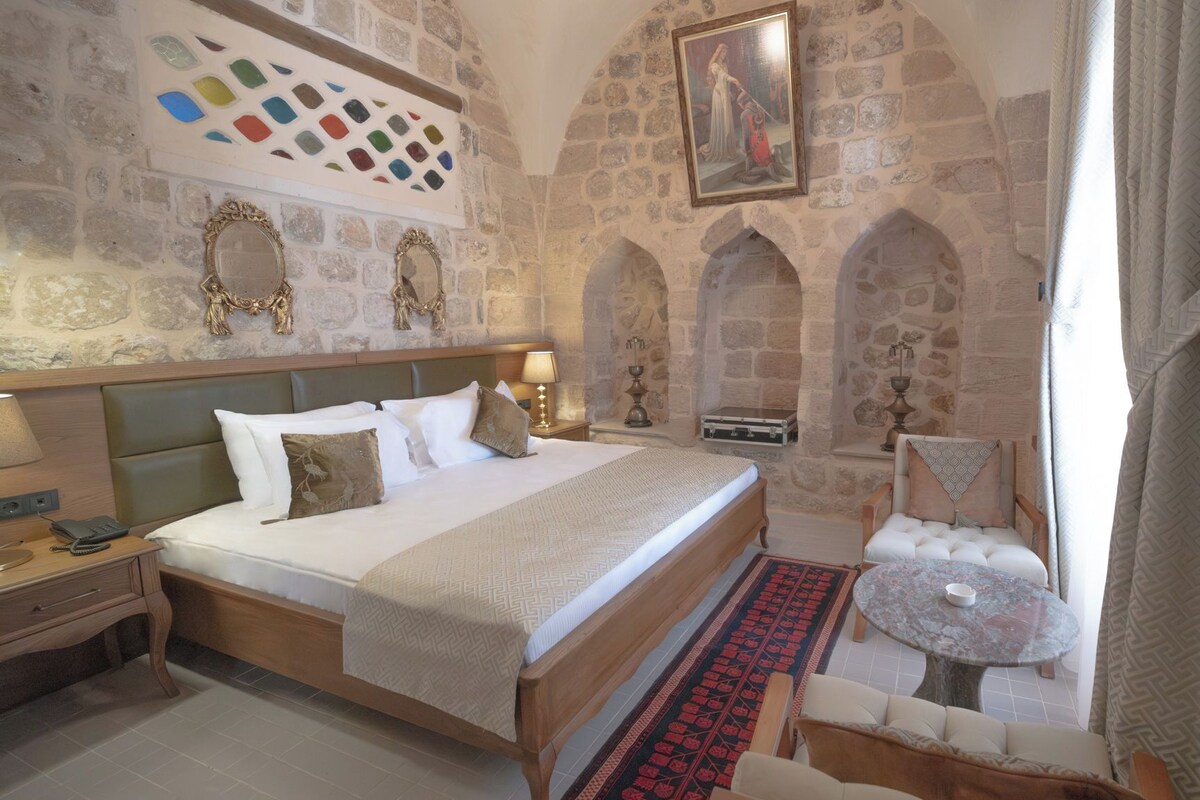 A traditional room with stone walls, a bed with a headboard, a small table, and a chair.