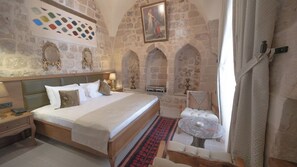 A traditional room with stone walls, a bed with a headboard, a small table, and a chair. - swiss inn hotel authentic collection  (MARDİN)