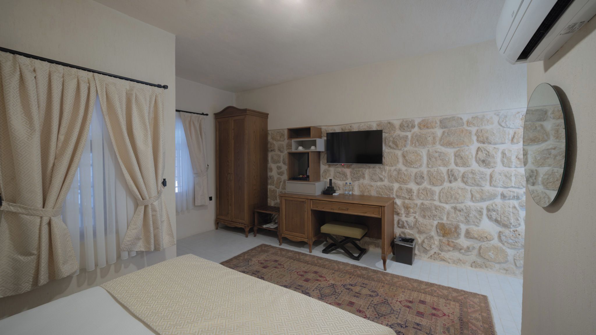 Un dormitorio con pared de piedra, un escritorio de madera, televisor y cama.