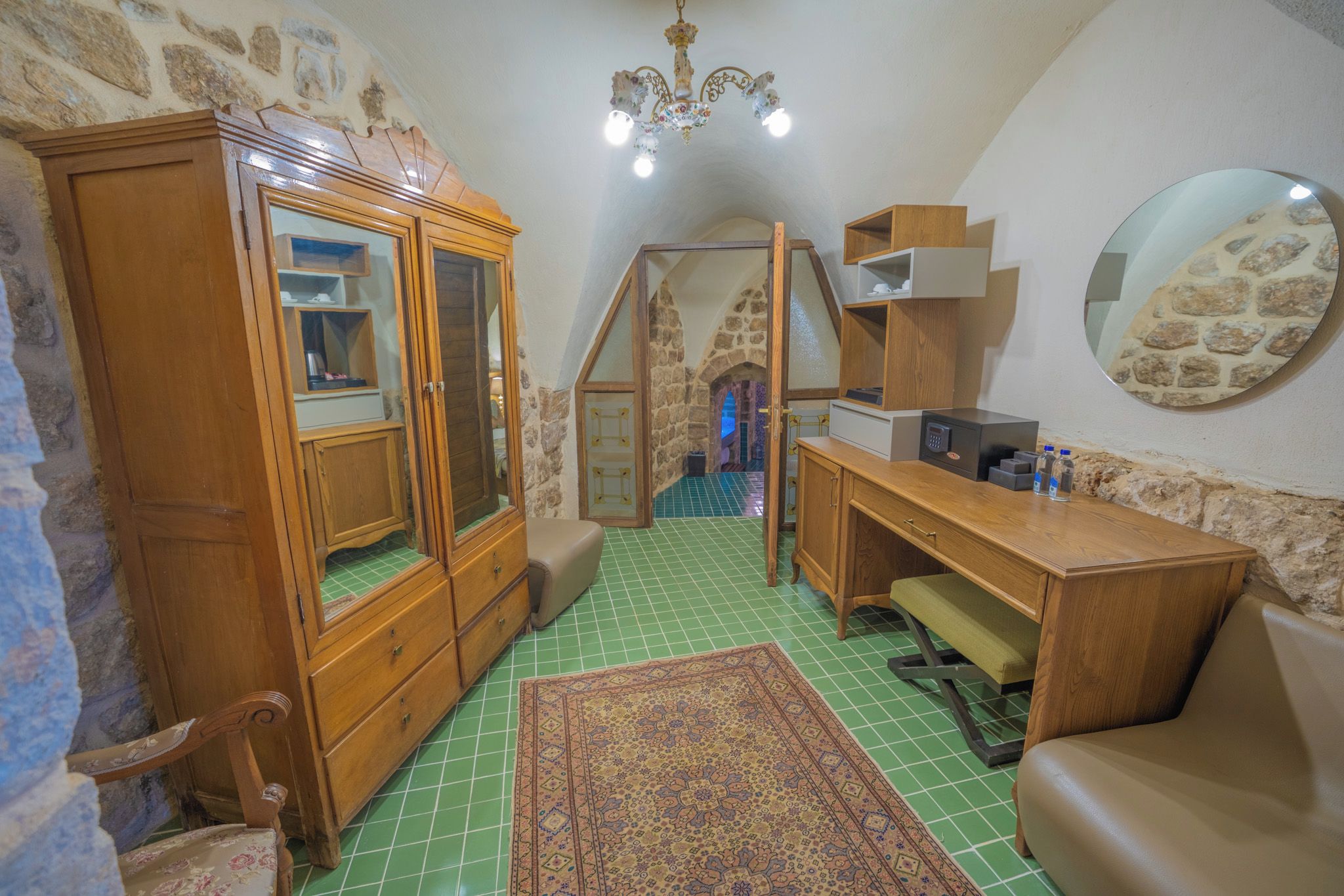 Een knus zolderkamertje met een houten garderobe, een bureau, een stoel en een spiegel aan de muur.