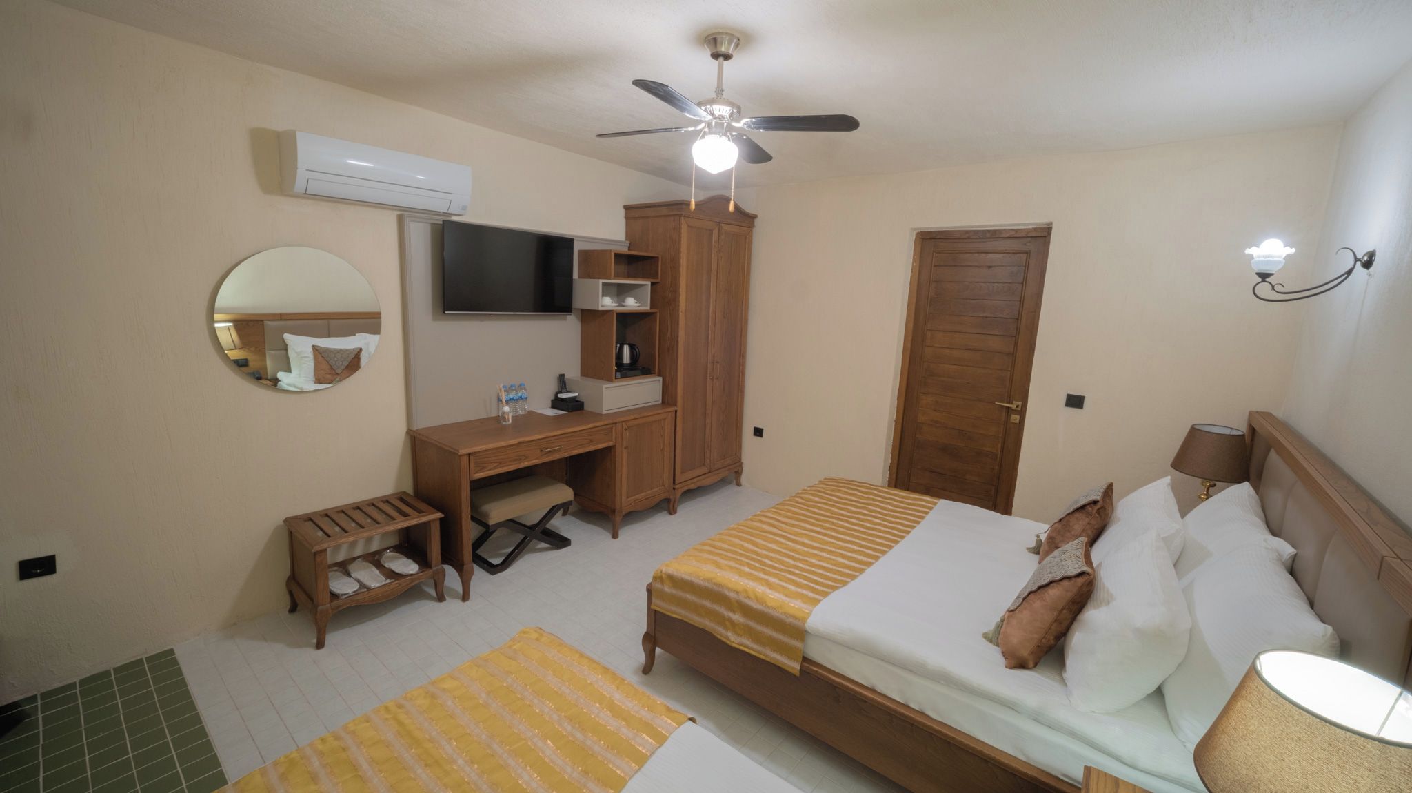 A hotel room with a bed, a desk, a wardrobe, a television, a ceiling fan, and a door.