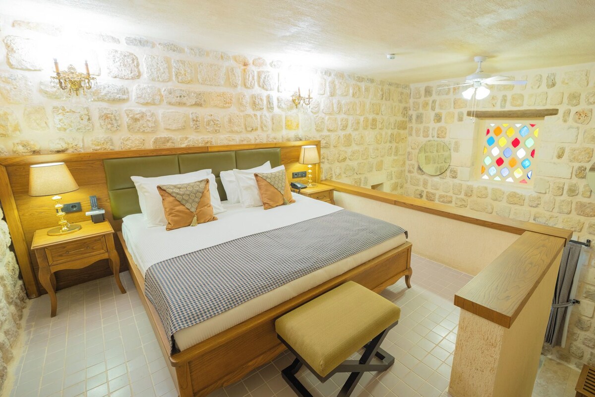 A hotel room with a stone wall, a wooden bed, a bench, and a small table.
