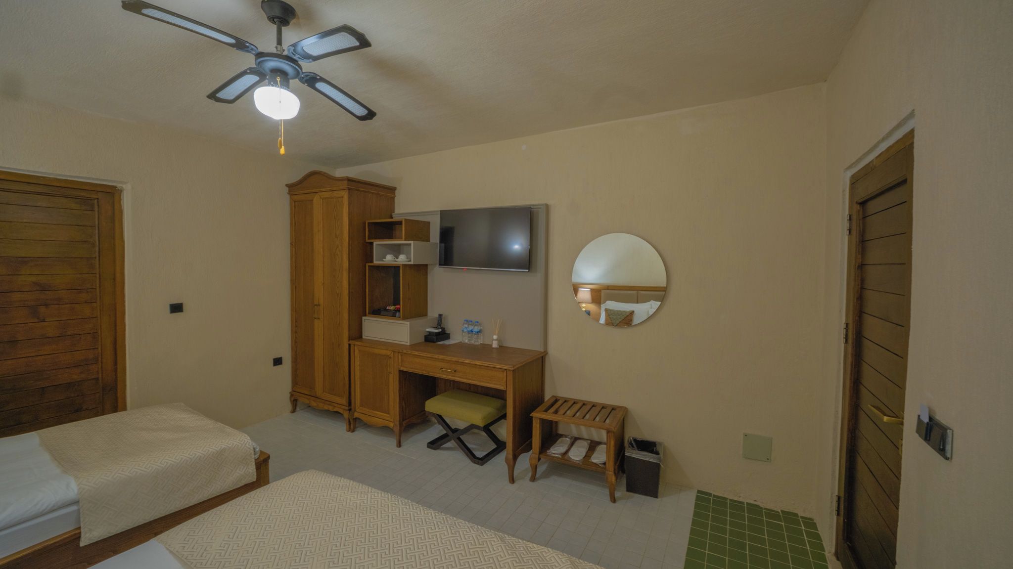 A bedroom with a bed, a desk, a chair, a wardrobe, a television, and a ceiling fan.