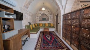 A cozy room with a stone wall, a green sofa, a wooden cabinet, and a decorative wooden panel with animal carvings. - swiss inn hotel authentic collection  (MARDİN)