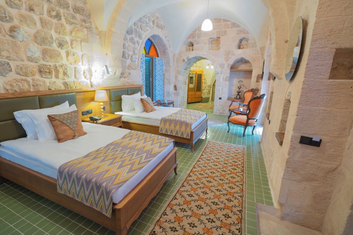 A hotel room with two beds, a stone wall, and a view of a courtyard.