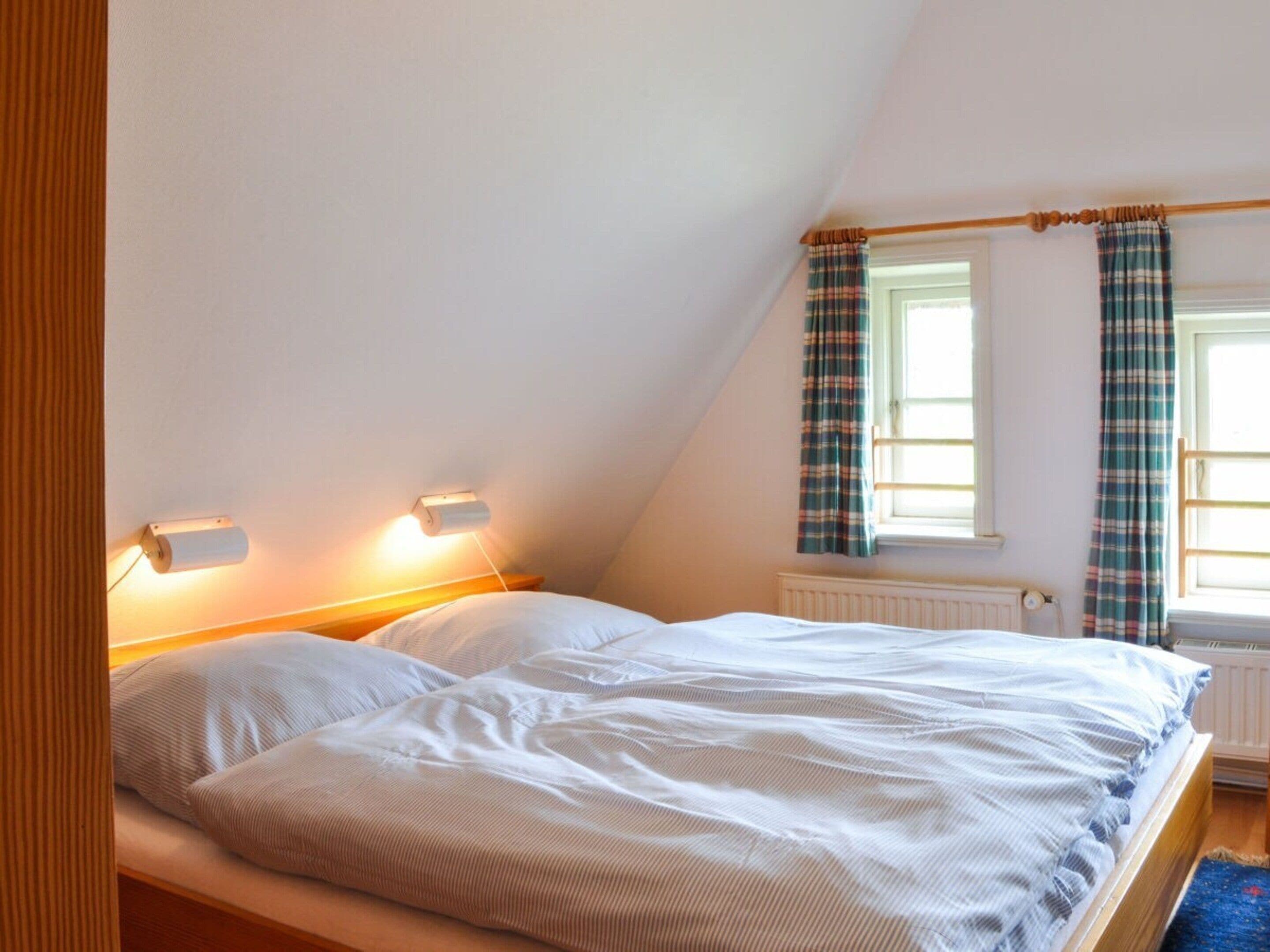 A bedroom with a bed, two bedside lamps, a window with curtains, and a radiator.