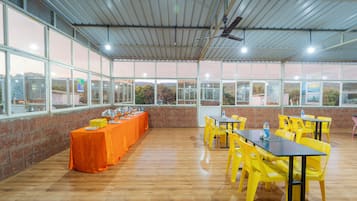 Un amplio espacio interior con una larga mesa cubierta con un mantel naranja brillante, rodeada de sillas amarillas.