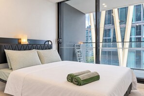Ein modernes Hotelzimmer mit einem grossen Bett, Blick auf die Stadt durch raumhohe Fenster und einem Balkon mit Metallgeländer.