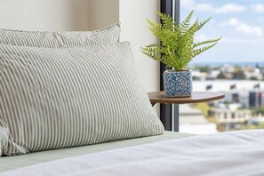 A bed with striped pillows and a potted fern on a bedside table. - Southbank 2BR 2Bath | 2 Queens & Free Parking (Southbank)