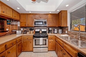 A kitchen with wooden cabinets, stainless steel appliances, and a window with blinds. - Steps from Snow Summit Resort! Ski In/Out Retreat! Incredible Views of Snow Summit Resort! (Big Bear Lake)