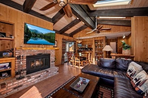 A cozy living room with a fireplace, leather sofa, and a television mounted on the wall. - Steps from Snow Summit Resort! Ski In/Out Retreat! Incredible Views of Snow Summit Resort! (Big Bear Lake)