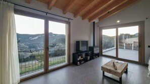 Uma sala de estar ampla com uma grande porta de vidro deslizante que dá para uma varanda, uma televisão e uma mesa de centro de madeira.