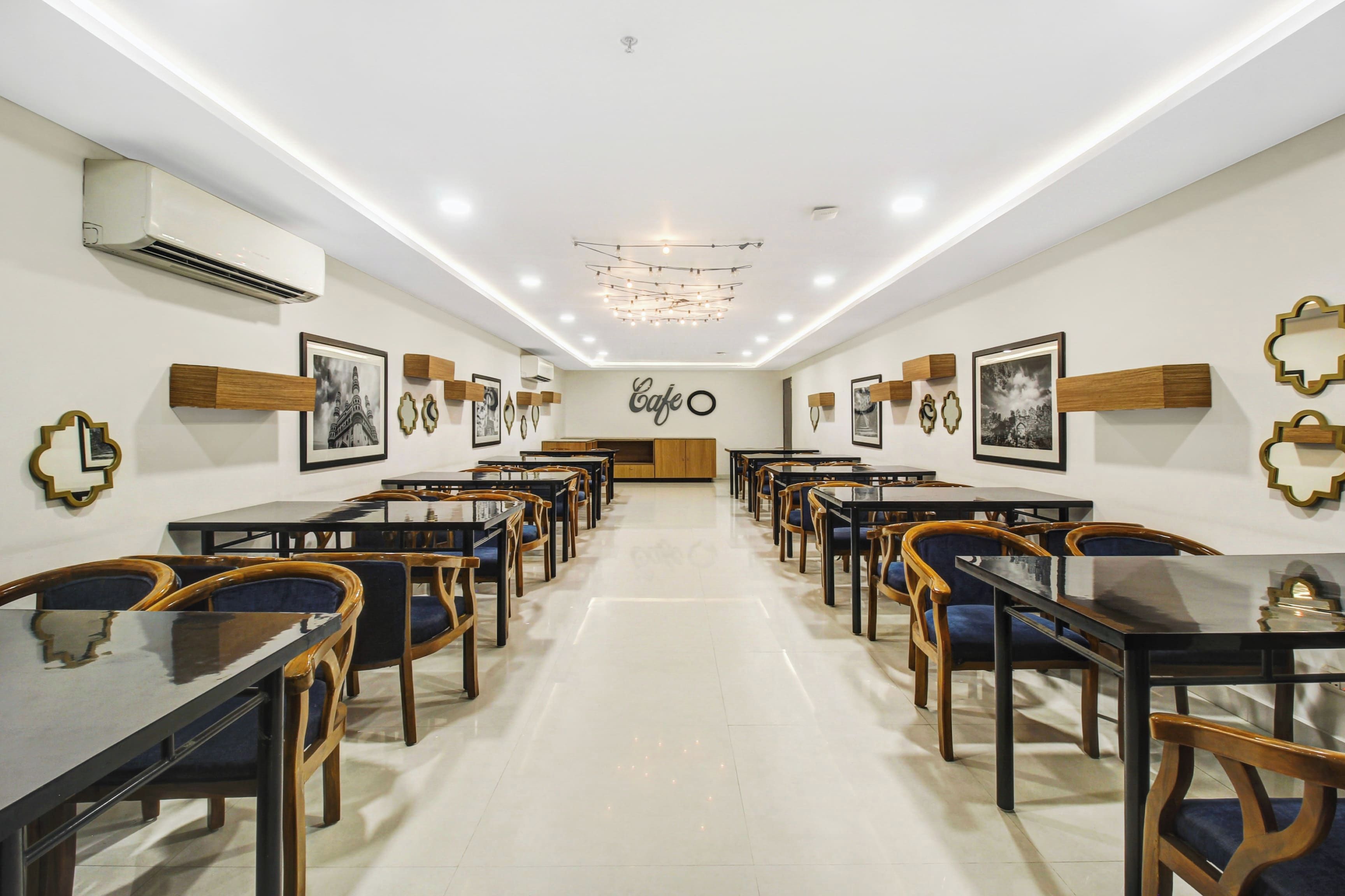 Uma ampla sala de jantar com mesas, cadeiras, um lustre e quadros nas paredes.