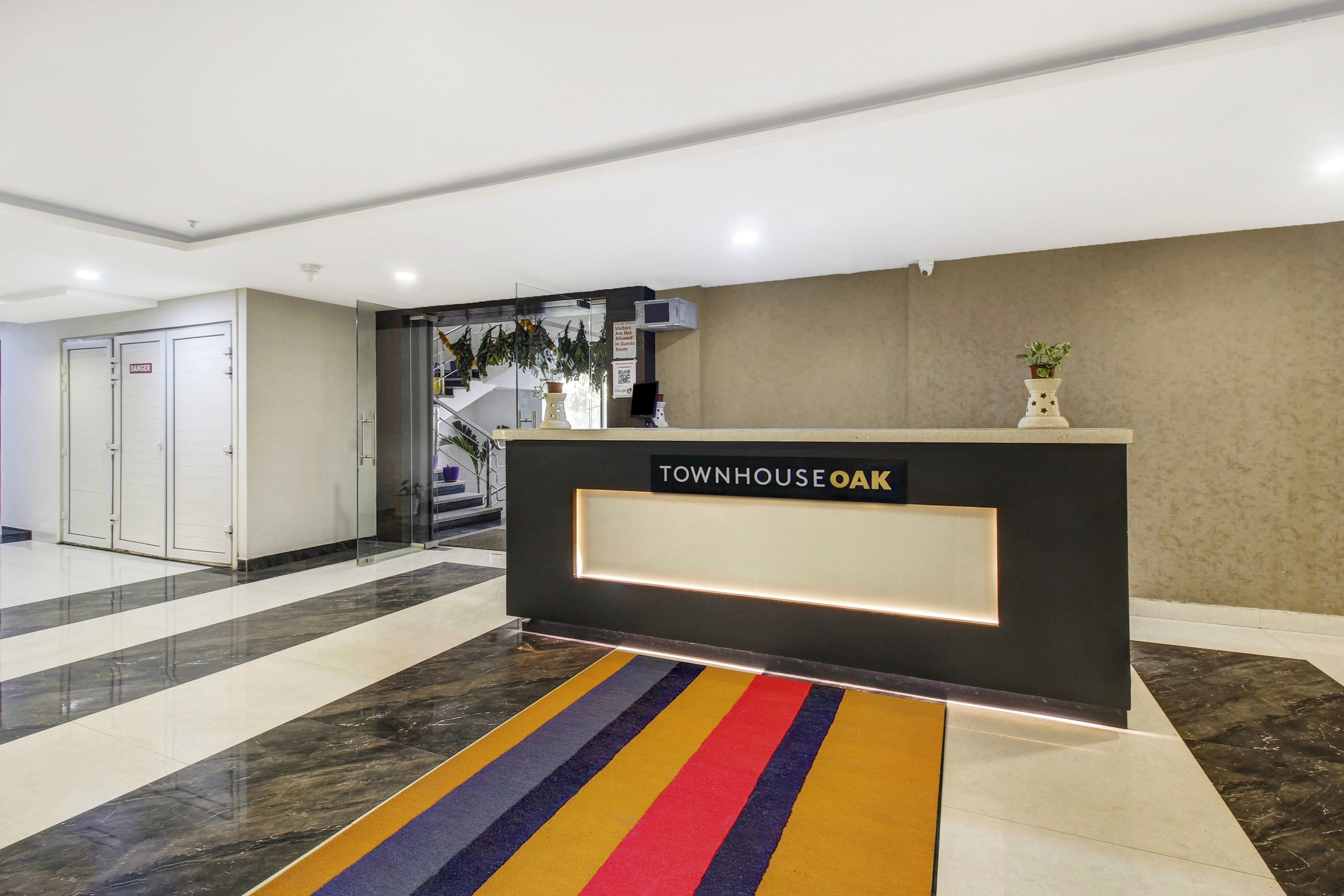 Balcão de recepção com uma placa indicando 'TOWNHOUSE OAK' em um saguão moderno com piso de mármore e entrada por porta de vidro.