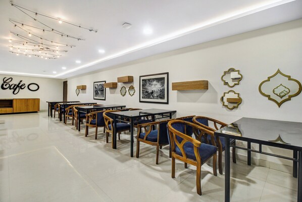 Interior de café com mesas, cadeiras, quadros nas paredes e um letreiro que diz 'Cafe'.