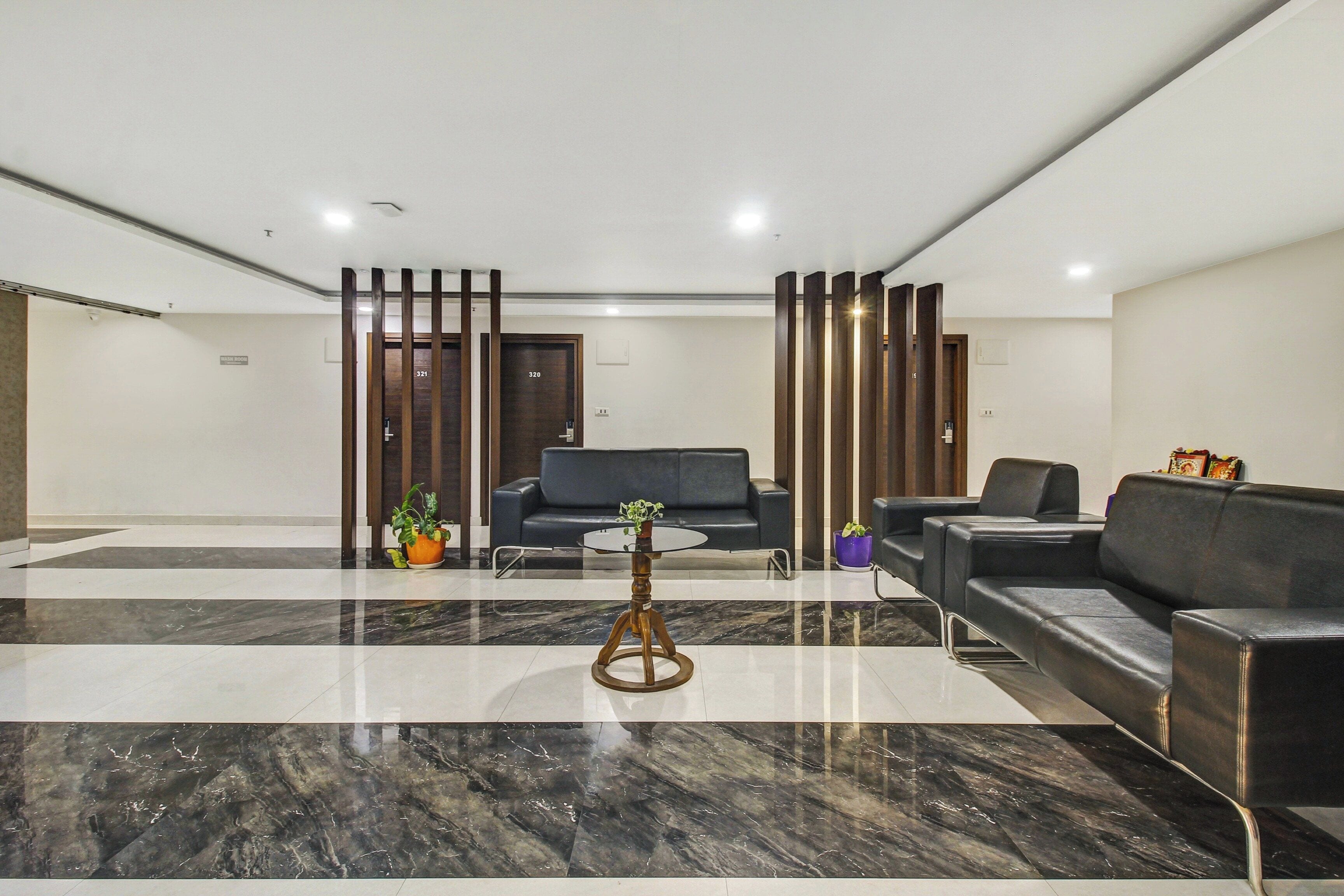 Um lobby moderno com piso de mármore, um sofá de couro preto, uma mesa de centro redonda e um balcão de recepção com divisória de madeira.