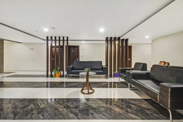 A modern lobby with a marble floor, a black leather sofa, a round coffee table, and a reception desk with a wooden partition.