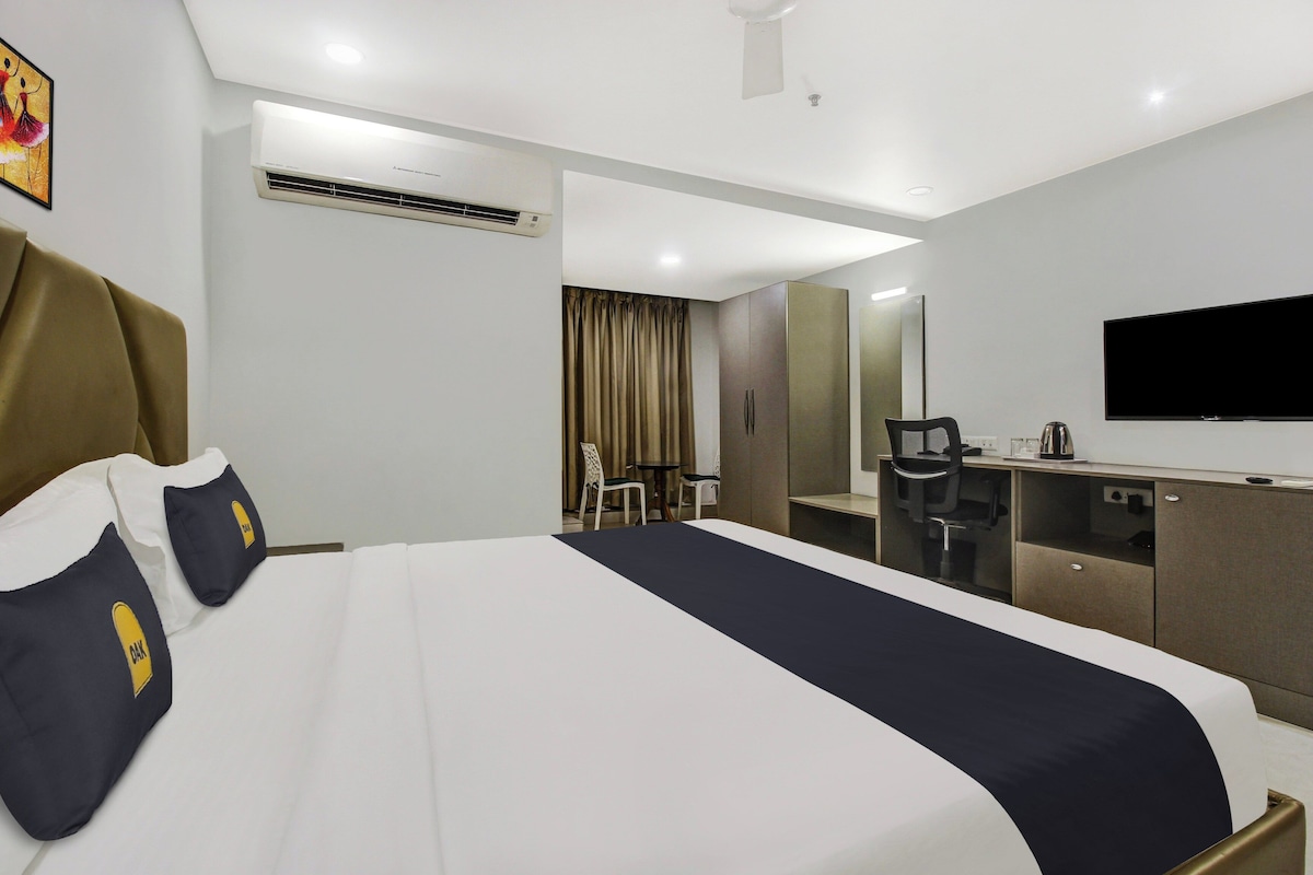Habitación de hotel con cama, escritorio, silla, televisor y aire acondicionado.