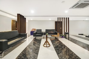 Um hall moderno com um sofá de couro preto, duas poltronas pretas, uma mesa de centro redonda de madeira e um chão de mármore.