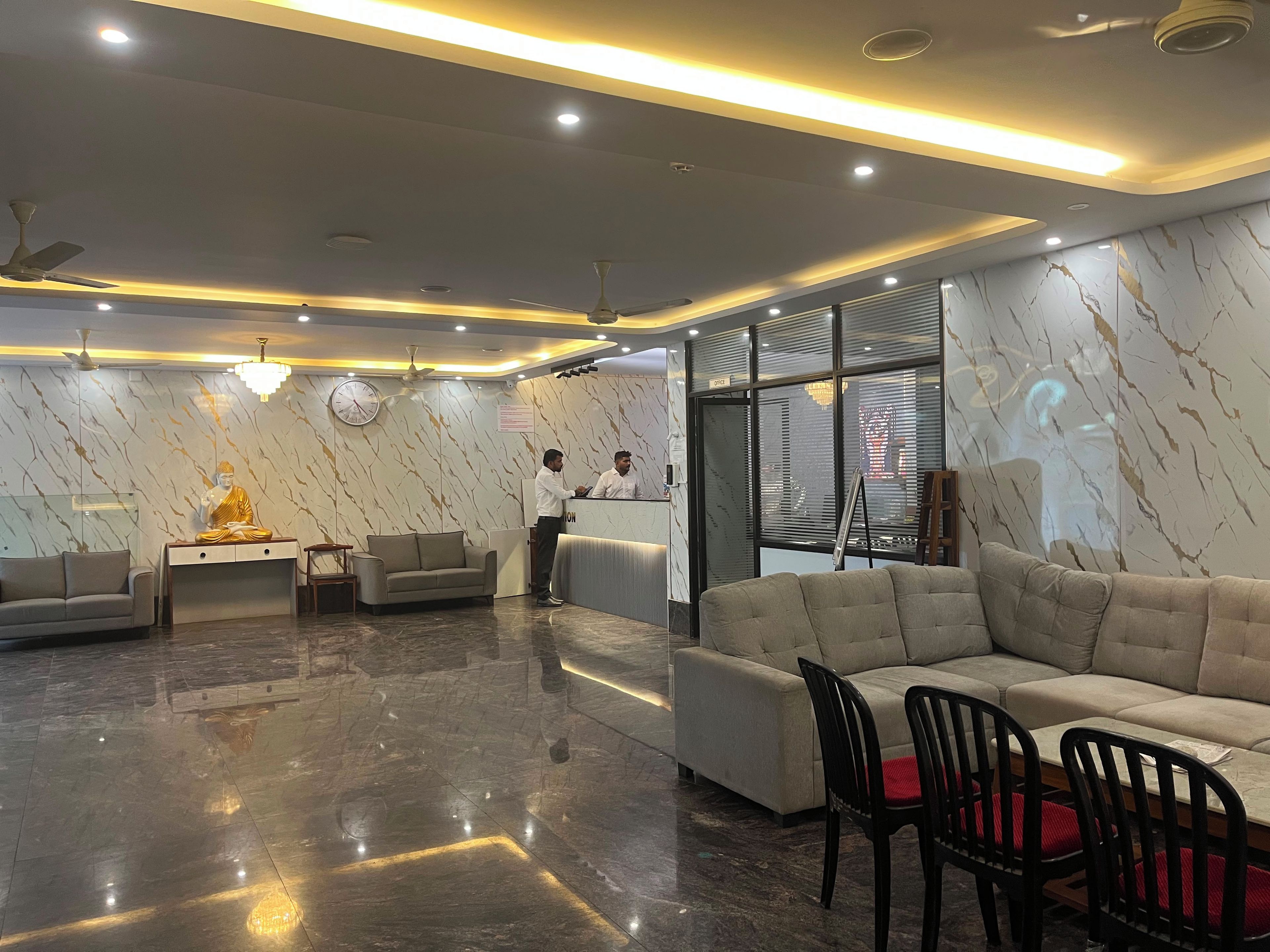 A modern lobby with marble walls, a reception desk, sofas, and a Buddha statue.