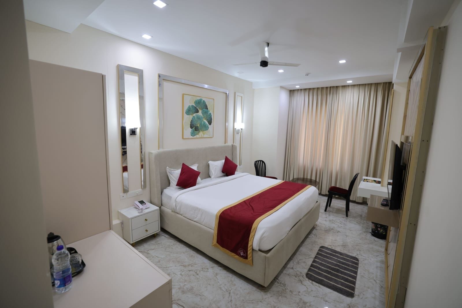A hotel room with a large bed, a desk, a chair, a television, and a ceiling fan.