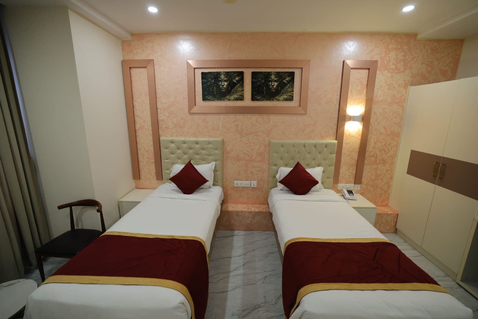 A hotel room with two beds, a wardrobe, a nightstand, and a chair.