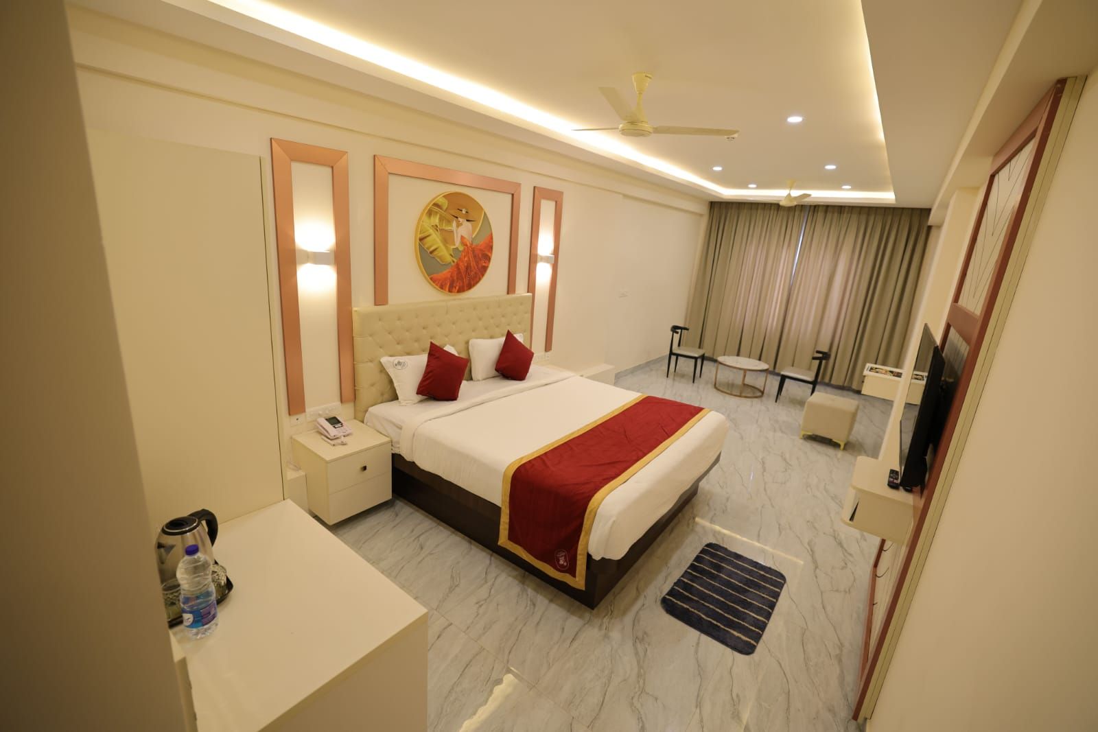 A hotel room with a bed, bedside tables, a desk, a chair, a television, and a ceiling fan.