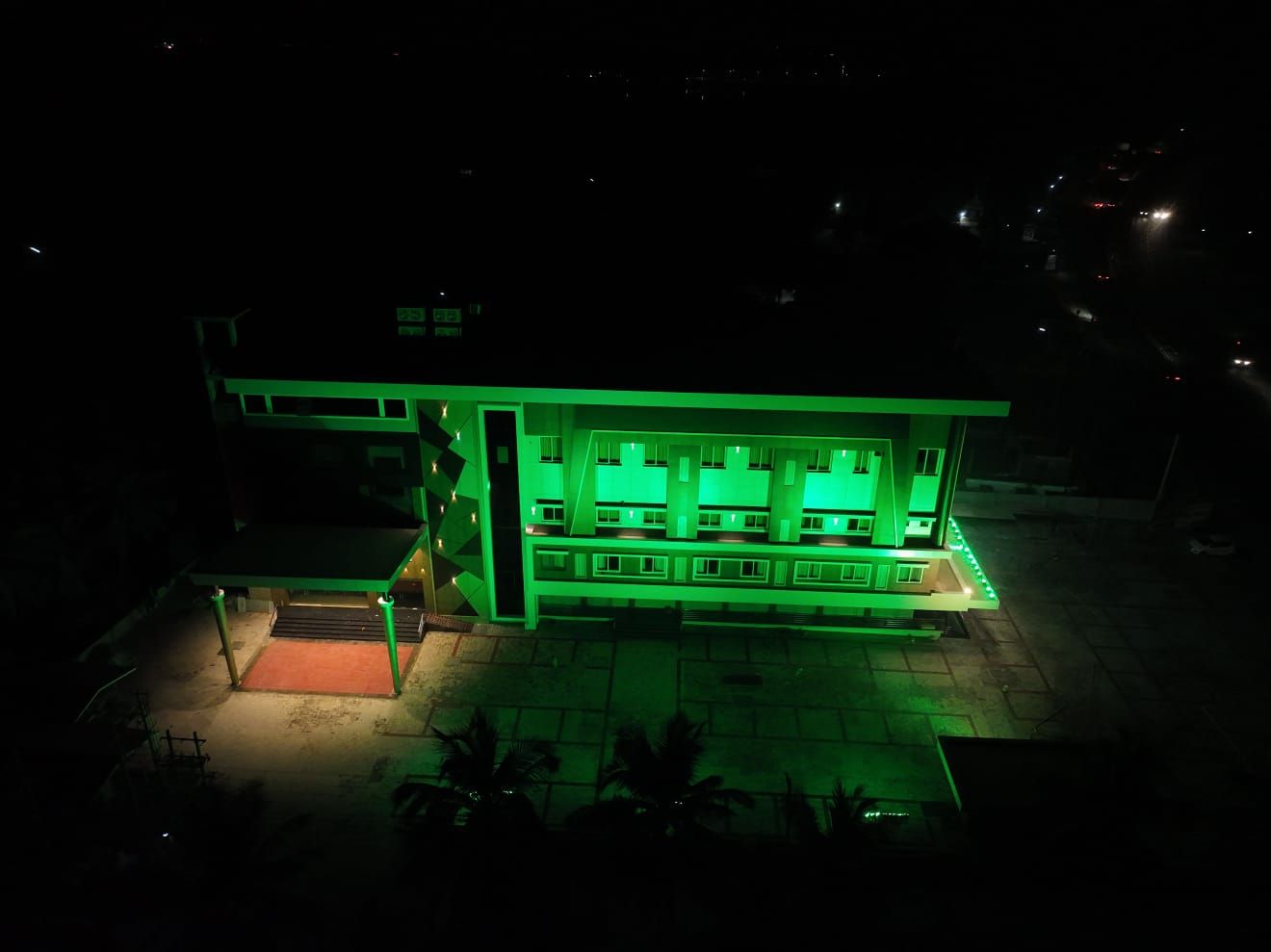 A building with multiple floors and a flat roof, illuminated by green lights.