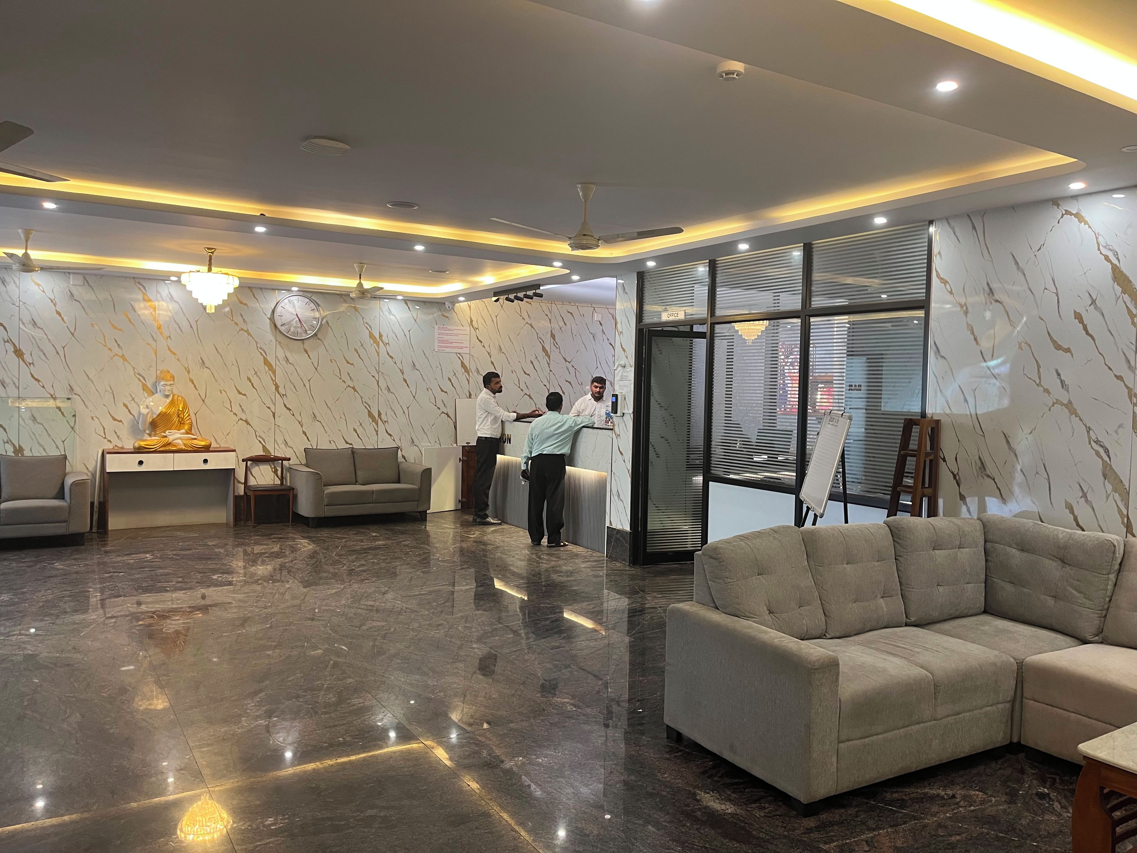 A reception area with a marble wall, a Buddha statue, a reception desk, and seating arrangements.