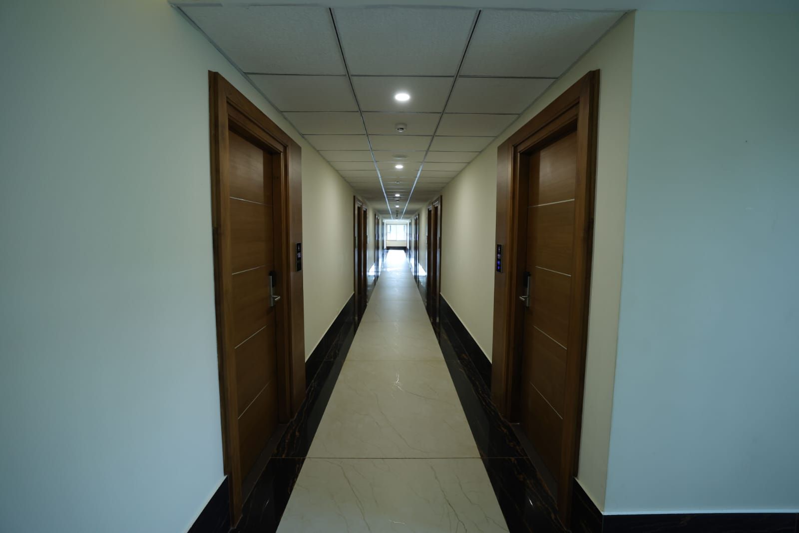 A long, narrow hallway with doors on both sides, leading to a bright room at the end.