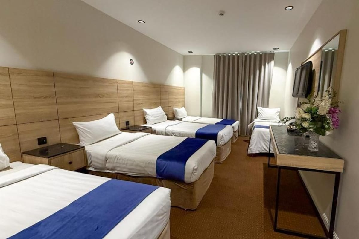 A hotel room with three beds, a desk, a mirror, and a TV.